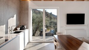 A modern kitchen with a large window, a flat-screen TV, and a dining area. - Studio 'Pai 521 Open Space' with Lake View, Wi-Fi and Air Conditioning (Torri del Benaco)