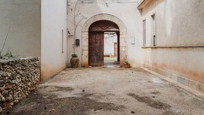 Un portail en arc donne accès à une cour intérieure, bordée d’un côté par un mur de pierre et de l’autre par un bâtiment.