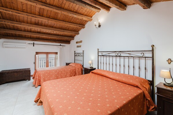 Una habitación con dos camas, vigas de madera en el techo, aire acondicionado de pared y una ventana con cortinas.