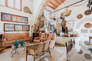 Un vaste espace de vie doté d’un plafond haut, d’un canapé, de fauteuils, d’une table à manger et de divers objets décoratifs.