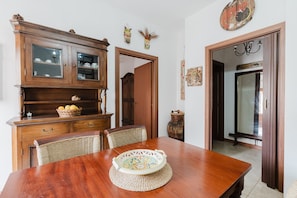 Un coin repas comprenant une table en bois, des chaises en osier, un meuble avec des portes en verre et un élément décoratif mural.