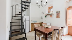 A dining area with a wooden table, wicker chairs, a chandelier, and a spiral staircase. - Apartment 'Torchio' with Shared Garden, Wi-Fi and Air Conditioning (Castelluzzo)