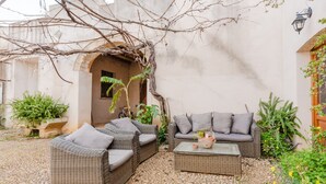 A courtyard with wicker furniture, a stone floor, and a wall with a window.