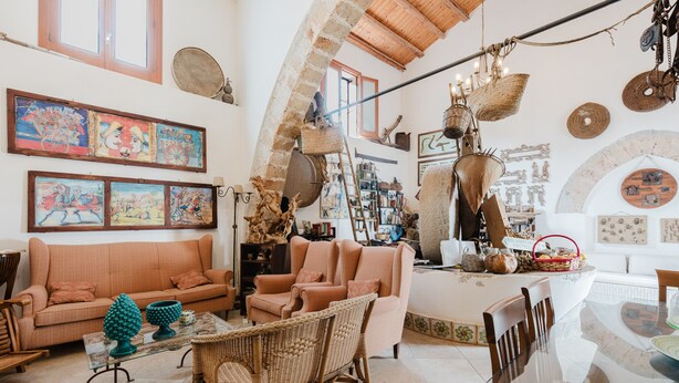 A spacious living area with a high ceiling, a sofa, chairs, a dining table, and various decorative items.