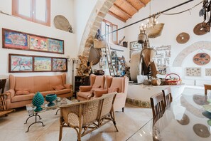 A spacious living area with a high ceiling, a sofa, chairs, a dining table, and various decorative items.