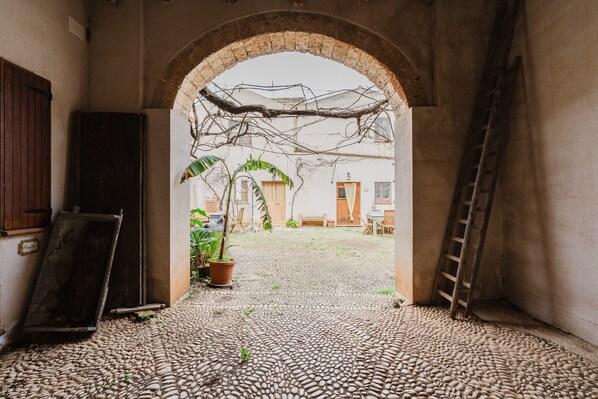 An arched doorway leading to a courtyard with cobblestone flooring, a ladder, and a potted plant.