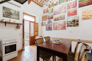 A dining area with a wooden table and wicker chairs, a white oven, and a wall adorned with landscape paintings.