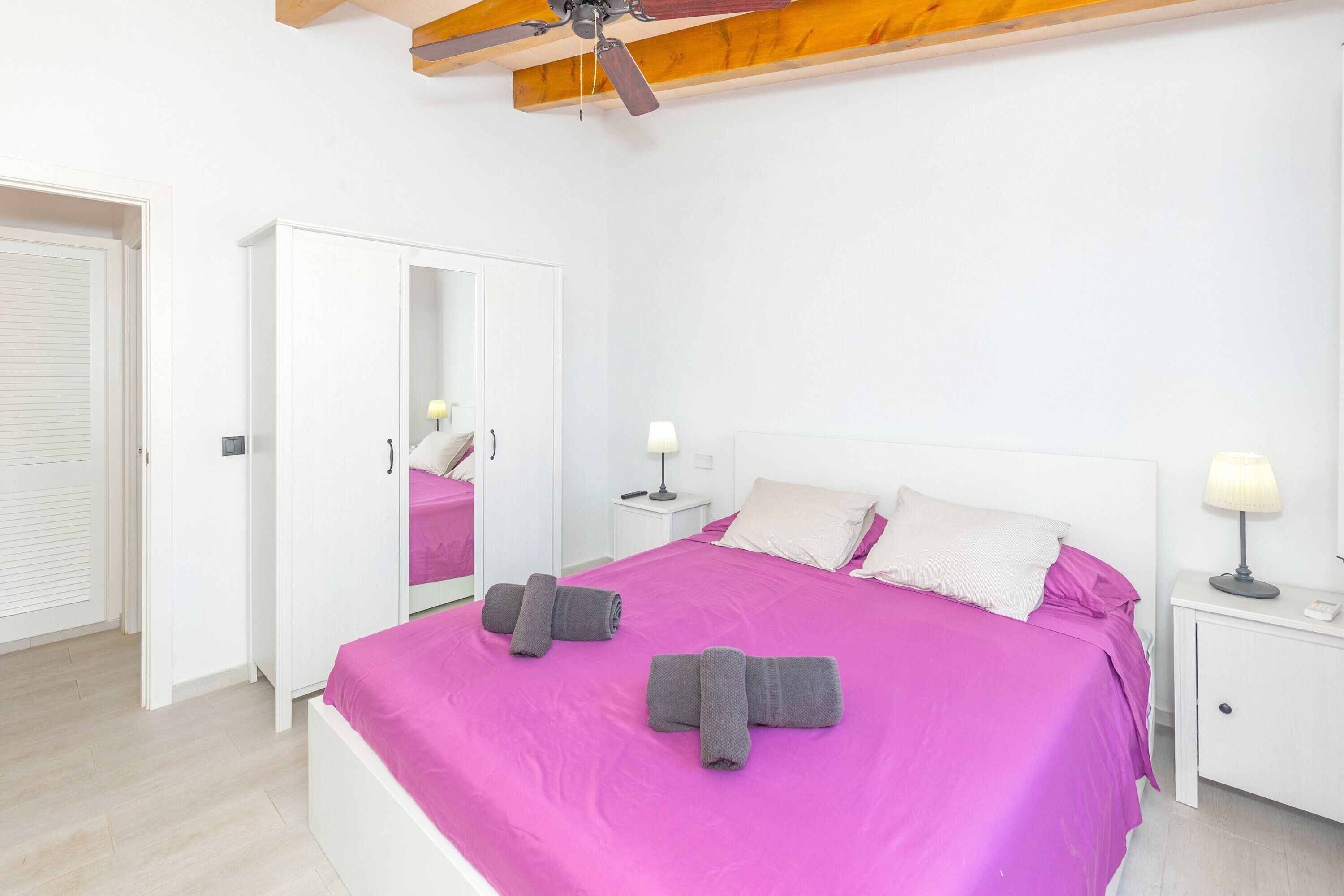 A bedroom with a bed, a wardrobe, a mirror, a ceiling fan, and bedside lamps.