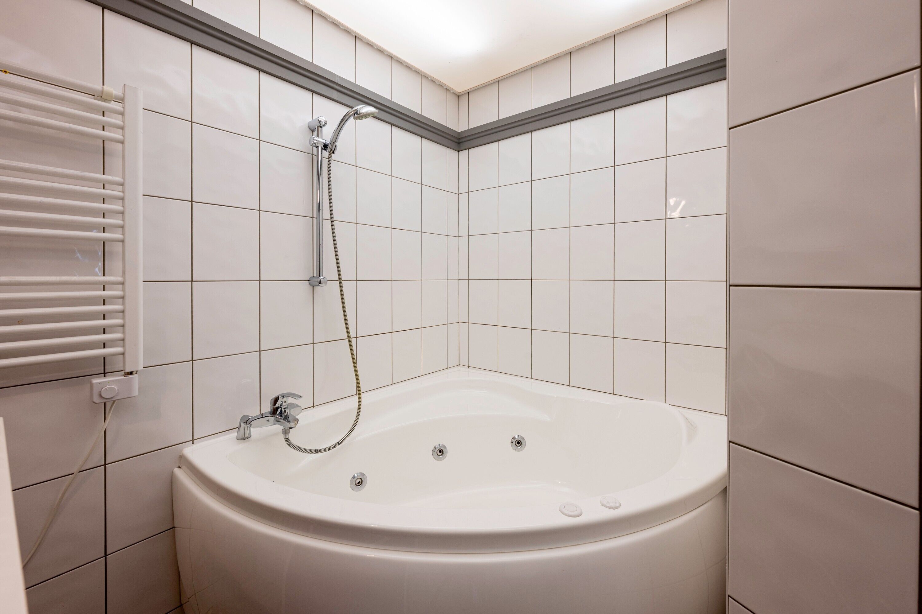 Une salle de bain avec une baignoire blanche, une douchette et un porte-serviettes fixé au mur.
