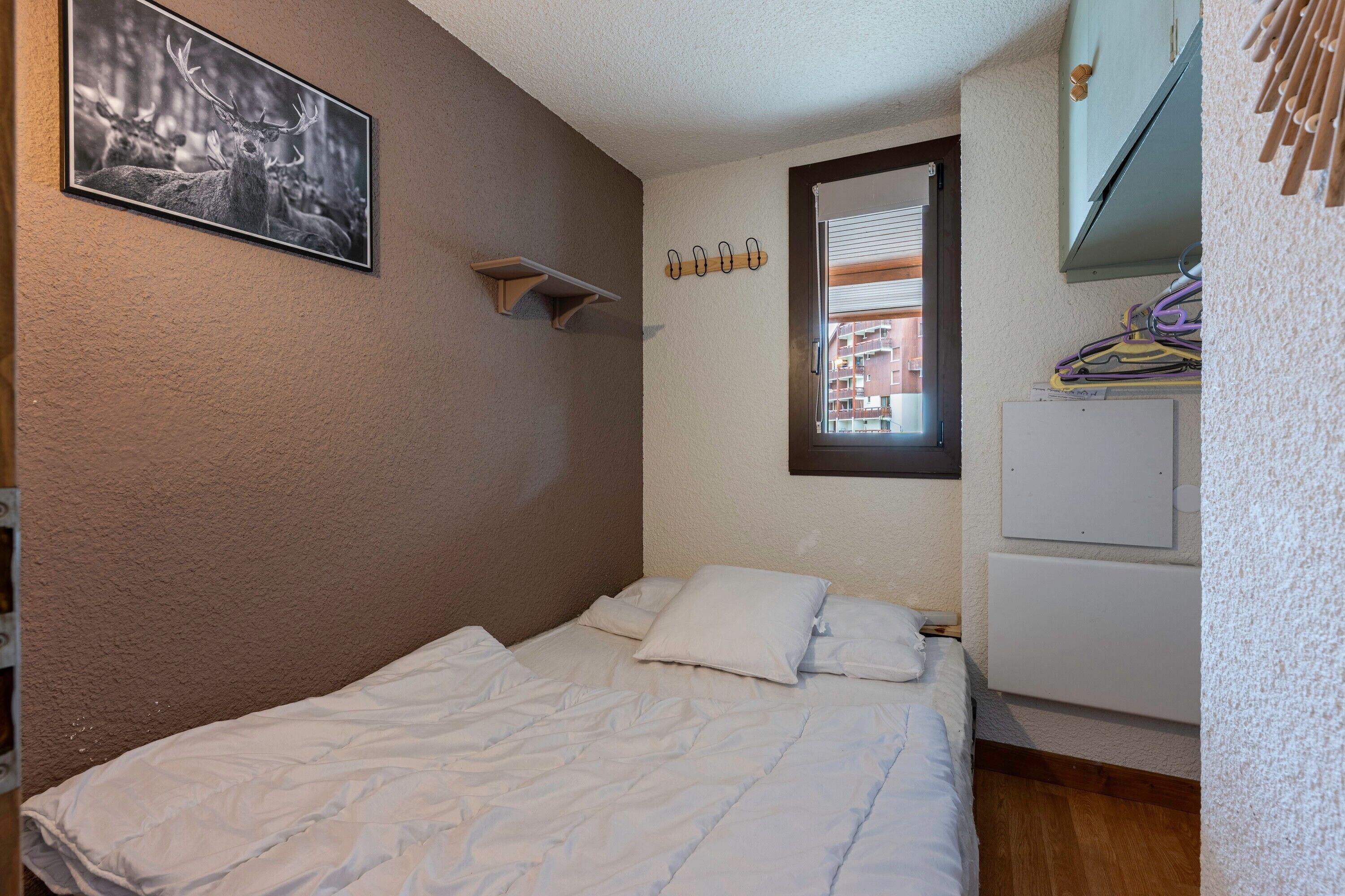 Ein Schlafzimmer mit Bett, Fenster, Kleiderständer und Wandregal.