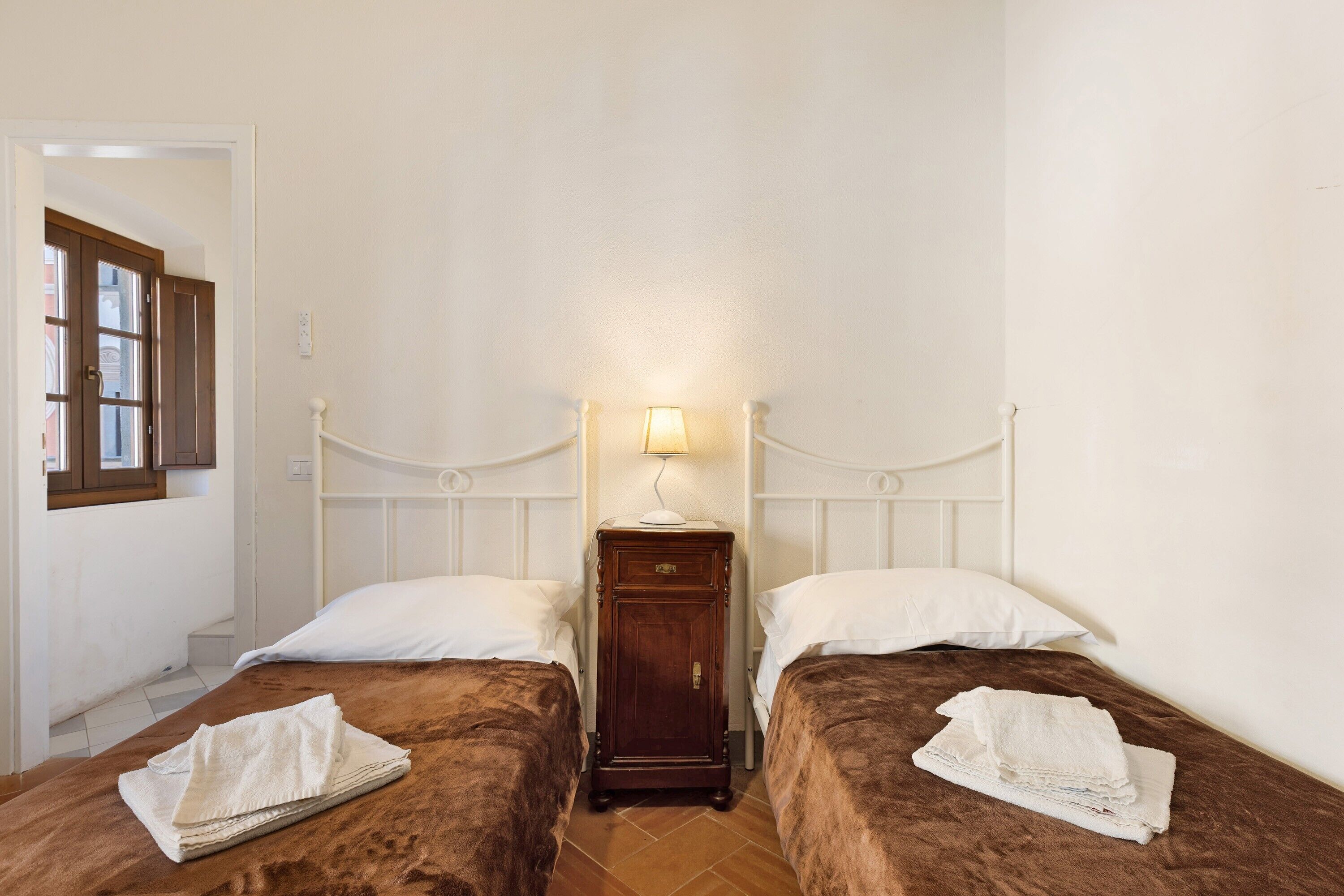 Een slaapkamer met twee bedden, een nachtkastje met een lamp en een raam met uitzicht.