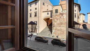 Vista a través de una ventana que muestra una calle con edificios, una escalera y coches aparcados.