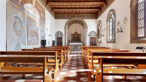 Interior de iglesia con bancales de madera, suelo de patrón hexagonal y altar central.