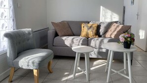 A living room with a grey sofa, a grey armchair, a small white table, and a potted plant.