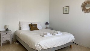A neatly made bed with white bedding and a zebra-patterned pillow, a bedside table with a lamp, and a wall-mounted mirror.