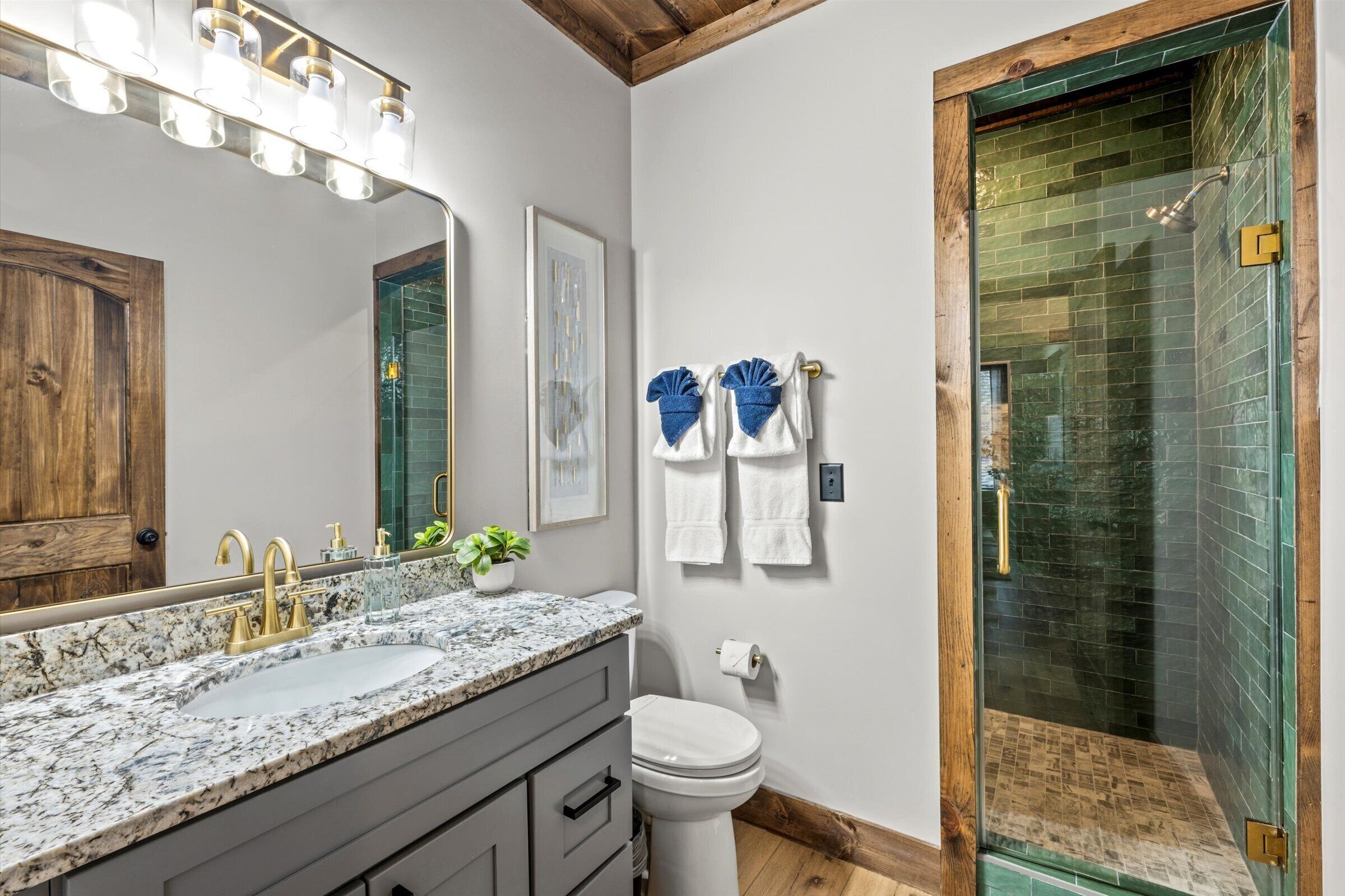 Une salle de bain avec un lavabo en marbre, un meuble-lavabo en bois, un grand miroir, une douche avec des portes en verre et un tableau encadré au mur.