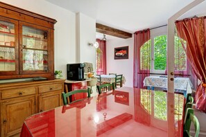 A dining area with a glass table, wooden cabinets, and a view through a window with curtains. - Room 'Ortensia' with Mountain View, Shared Pool and Wi-Fi (Fontona)