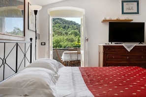 Ein Schlafzimmer mit Bett, Schminktisch, Fernseher und einem Balkon mit Tisch und Stuhl.