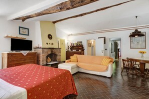 Ein Zimmer mit Bett, Sofa, Kamin, Fernseher, Holzbalken und einem Essbereich.