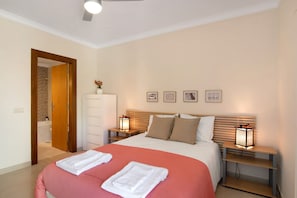 Habitación de hotel con cama, dos mesitas de noche con lámparas, cabecero de madera, armario y puerta que da a un baño.