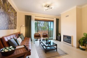 Un salon comprenant un canapé, deux fauteuils, une table basse, une cheminée et un balcon avec des rideaux.