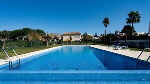 A rectangular swimming pool with clear blue water, surrounded by a white deck, palm trees, and a house in the background. - Apartment 'Condomínio Do Vale' with Shared Pool, Shared Terrace and Wi-Fi (Guia)