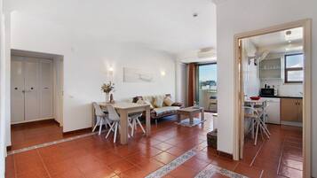 A spacious living area with a dining table, sofa, and kitchen area visible through an open doorway.