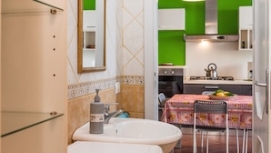 Une salle de bain équipée d’un lavabo, d’un miroir et d’articles de toilette. On aperçoit à l’arrière-plan un coin repas avec une table et des chaises.