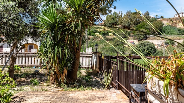 Un espace extérieur aménagé en terrasse, avec un sol en pierre, une clôture en bois et un palmier.