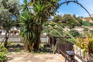 Un espace extérieur aménagé en terrasse, avec un sol en pierre, une clôture en bois et un palmier.