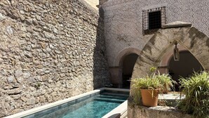 Un edificio de piedra con piscina, arcos y plantas en macetas.