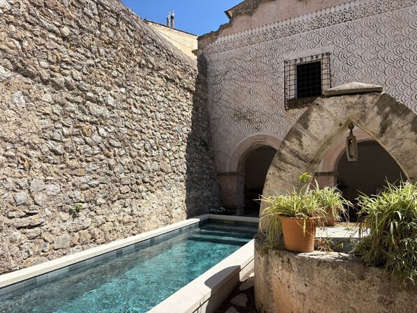Un bâtiment en pierre doté d’une piscine, de portes en arc de cercle et de plantes en pot.