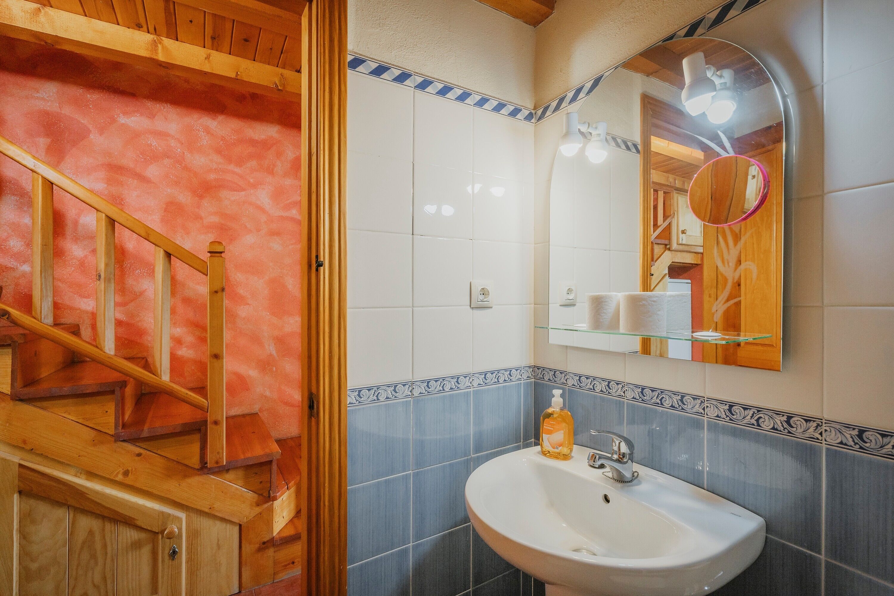 A bathroom with a wooden staircase, a white sink, and a mirror with a round frame.