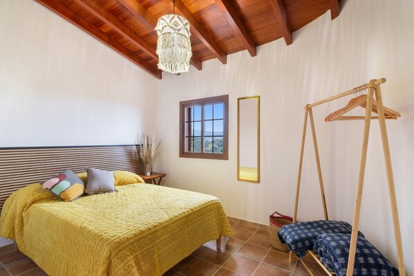 Ein Schlafzimmer mit einem Bett, einer Pendelleuchte, einer Holzschaukel, einem Fenster und einem Spiegel.