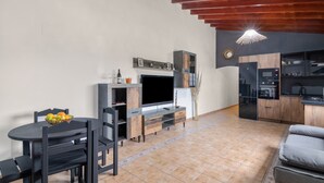 A modern living room with a TV, dining table, and chairs, a kitchen with cabinets and appliances, and a wooden ceiling. - 'Canarian Retreat' with Sea Views, Private Terrace and Wi-Fi (Santa Brigida)