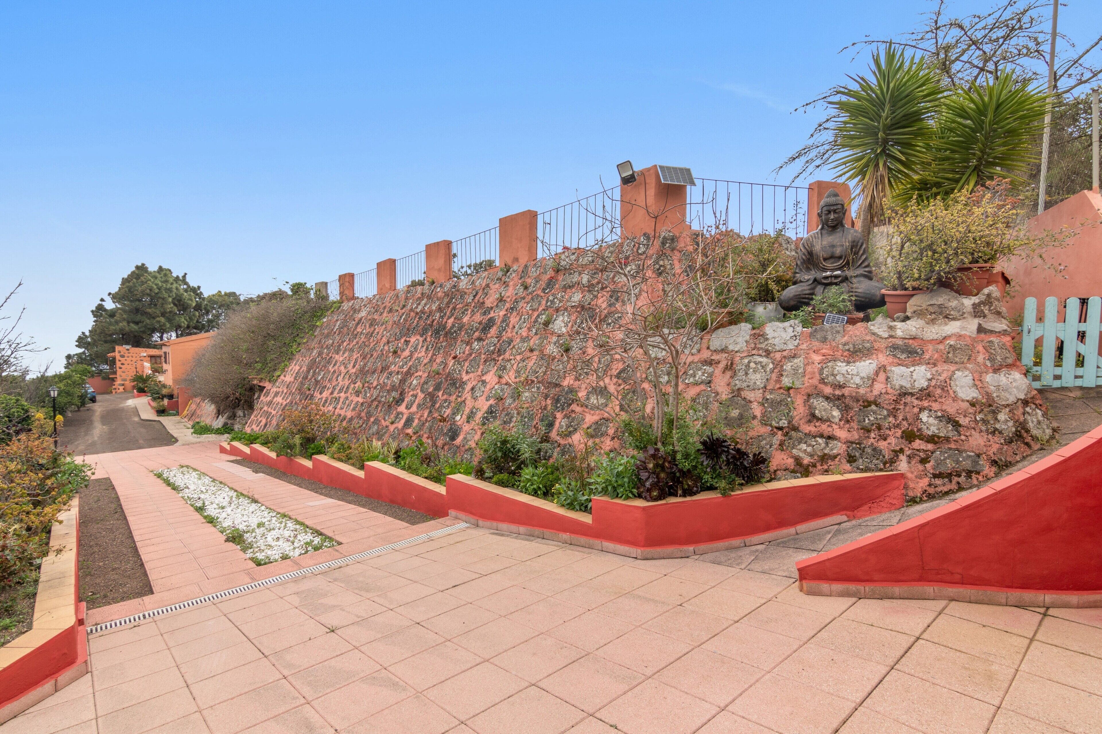 Un jardin en terrasses agrémenté d’une statue, avec des murs en briques rouges et un ciel dégagé.