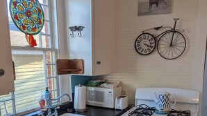 Una cocina con pileta, estufa y microondas. Se observa una ventana con un diseño de vitral, un reloj de pared y una decoración con bicicleta.