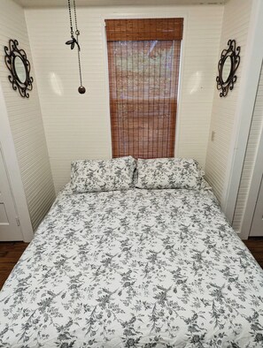 Une chambre à coucher avec une couvre-lit à motifs floraux, une fenêtre avec des stores et des miroirs décoratifs sur les murs.