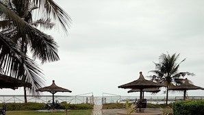 A stone pathway leading to beach umbrellas and chairs, surrounded by grass and palm trees. - beach resort casa (Sekondi-Takoradi)