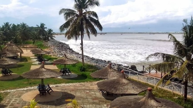 A beachside resort with thatched umbrellas, palm trees, and a view of the ocean. - beach resort casa (Sekondi-Takoradi)