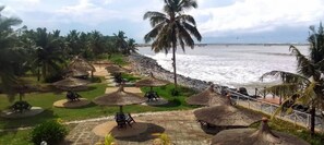 A beachside resort with thatched umbrellas, palm trees, and a view of the ocean. - beach resort casa (Sekondi-Takoradi)