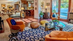 A spacious living room with a sofa, ottoman, and coffee table, a kitchen area with wooden cabinets, and a dining area with chairs.