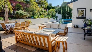 An outdoor patio with wooden furniture, a table, and a pool in the background.