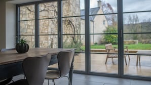Ein moderner Essbereich mit großem Tisch und Stühlen, große Fenster mit Blick auf Garten und Haus.