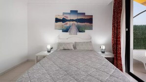 Un dormitorio con cama, dos mesitas de noche, una lámpara de noche, un ventanal con cortinas y un cuadro colgado en la pared.