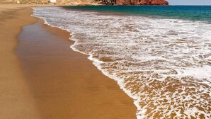 Una playa con orilla arenosa y una colina rocosa al fondo.