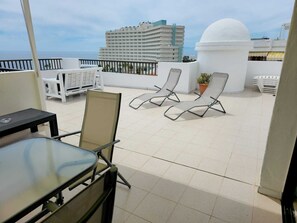 Eine Dachterrasse mit Tisch und Stühlen, einer weißen Kuppelkonstruktion und Blick auf ein Hotelgebäude.