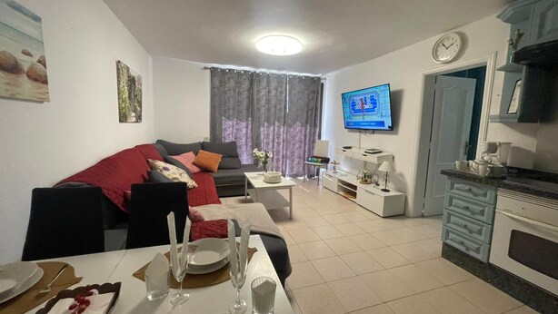 Un salón con sofá, televisor, comedor y zona de cocina.