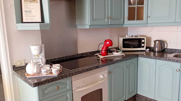 A kitchen with teal cabinets, a microwave, a kettle, and a coffee maker.