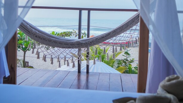 A hammock on a wooden deck overlooking a beach with a view of the ocean. - Luma at the beach (Santa Marta)